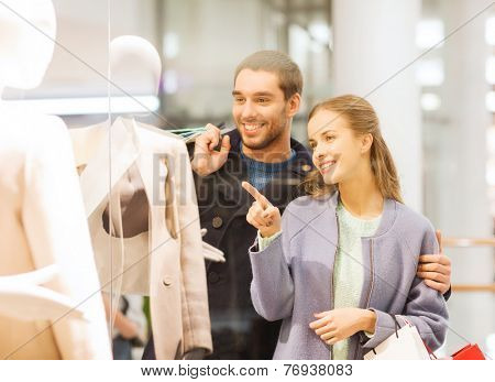 sale, consumerism and people concept - happy young couple with shopping bags pointing finger to shop window in mall