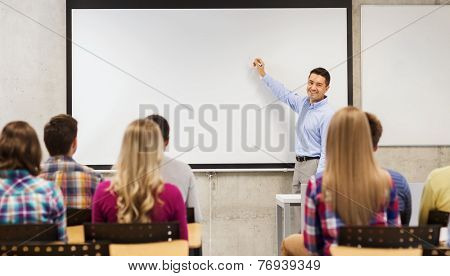 education, high school, teamwork and people concept - smiling teacher standing in front of students and writing something on white board in classroom