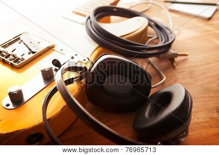 Guitar recording scene. An electric guitar, memo pad , and a professional grade headphones on a rustic or bare wooden table, with by-the-window type warm light. 
