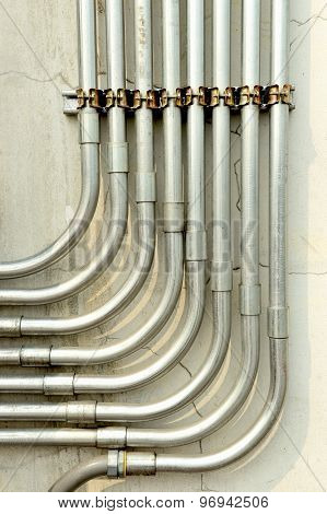 Aluminum tubing for wire protection lined up on old concrete wall .