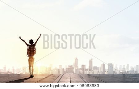 Rear view of girl with hands up facing sunrise abone city