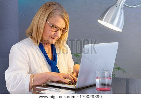 Close up portrait of senior woman socializing on laptop at home.Woman typing on computer at table.