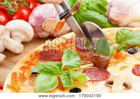 Hot pizza slice with melting cheese mushrooms and salami on a rustic wooden table. Cutting the knife into pieces slices