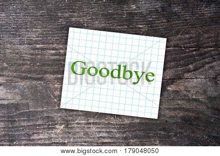 Goodbye Text On A Checkered Note. Wooden Background
