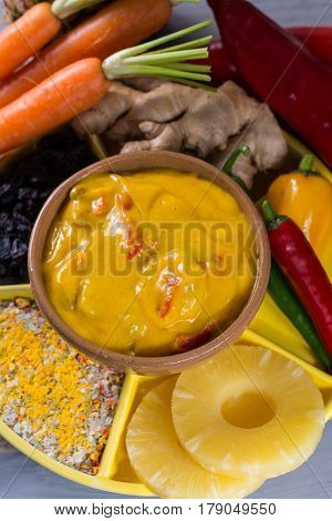Bowl of vegetable curry sauce and ingredients that go into making it - paprika chili pepper carrot pineapple gember. Used widely in Indian food.