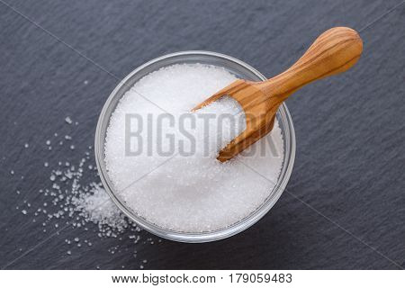 birch sugar xylitol in a wooden scoop and glass bowl on black background closeup