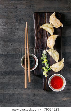 Gyozas potstickers on lettuce salad with sauces. Served in traditional china plate with chopsticks and spring onion on wood serving board over old metal background. Top view, space. Asian dinner