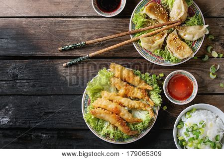 Fried tempura shrimps and gyozas potstickers on lettuce salad with sauces and rice. Served in traditional china plate with chopsticks over old wooden background. Top view. Asian dinner