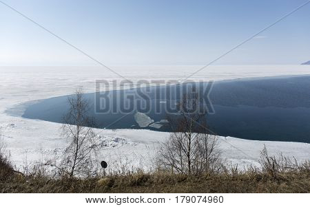Baikal lake spring landscape view. Snow-covered shore of the lake. Rocky forested coastline. Boundary of ice and open water