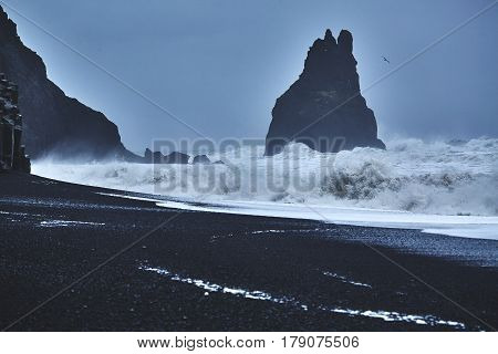 Reynishverfisvegur, Reynisfjara black sand beach with rocks, ocean and dark rain and storm clouds near the village of Vik in Iceland.