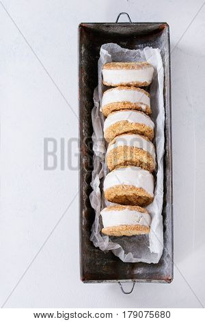 Set of homemade ice cream sandwiches in oat cookies with almond sugar crumbs on baking paper in old metal bowl over gray texture background. Top view with space