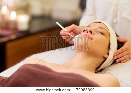 people, beauty, cosmetology and treatment concept - close up of beautiful young woman lying with closed eyes and cosmetologist applying facial mask by brush at spa