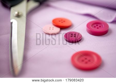 needlework and tailoring concept - scissors, sewing buttons and cloth