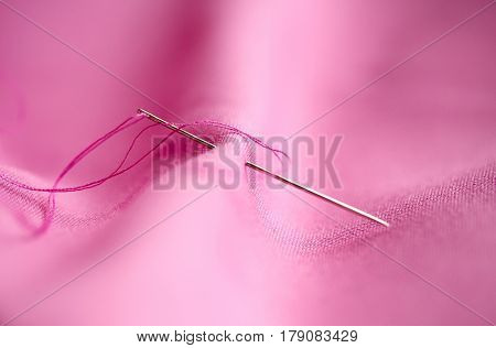 needlework and tailoring concept - sewing needle with thread stuck into pink fabric