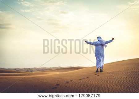 Arabian man walking in the desert at sunrise
