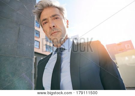 Portrait of businessman waiting outside building, leant on wall
