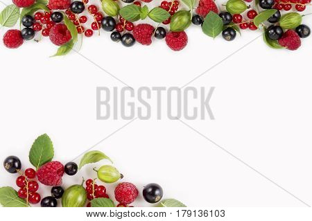 Various fresh summer berries on white background. Ripe raspberries currants gooseberries mint and basil leaves. Berries at border of image with copy space for text. Background berries.