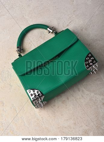 Nice beautiful small womans leather green fashionable bag with decorative metallic spikes or thorns on white textured background