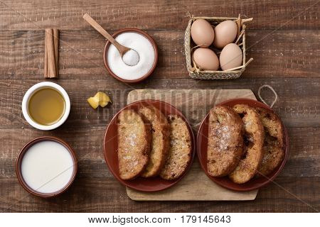 high-angle shot of a rustic wooden table with torrijas, typical spanish dessert eaten in Lent and Easter, and the ingredients to prepare it, such as eggs, cinnamon, milk, sugar or olive oil