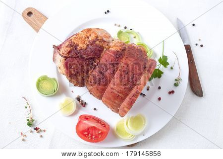 Rolled stuffed roast pork with spices on a white plate.