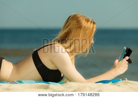 Summertime pleasures enjoying vacation concept. Woman in bikini sunbathing and relaxing on beach using smartphone checking social media and writing sms