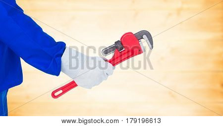 Digital composite of Mechanic arm with wrench against blurry yellow wood panel