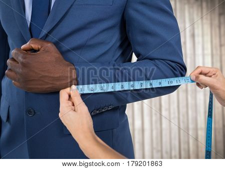 Digital composite of Man in suit mid section being measured against blurry wood panel