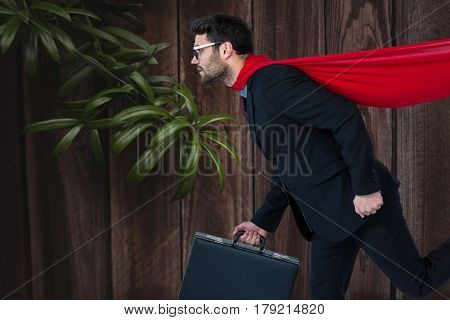 Digital composite of Confident business man super hero walking against wooden background with leaves