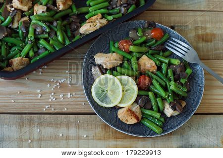 Portion of green beans with cherry tomatoes chicken breasts mushrooms sesame seeds and lemon served on wooden table. Healthy eating concept