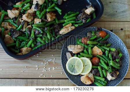 Baked green beans chicken breast red cherry tomatoes mushrooms served on grey plate with sesame seeds and sliced lemon