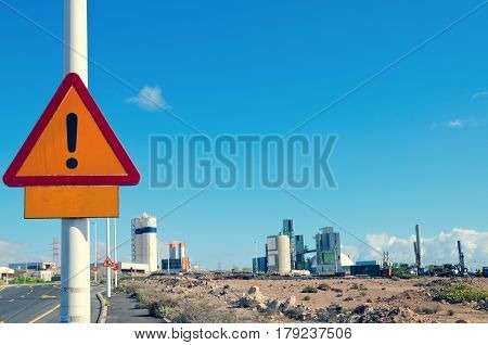 Warning road sign against a blue sky and industrial plant on background. Punta de Abona Tenerife. Canary Islands Spain.