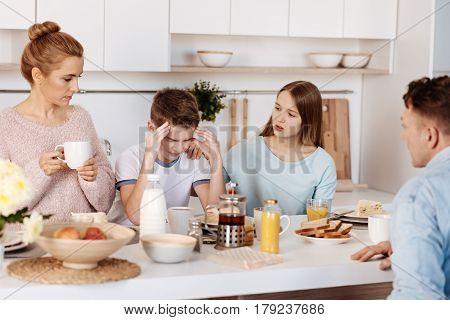 Dont feel depressed. Moody cheerless boy sitting at the table and his sister supporting him while having meal with their parents