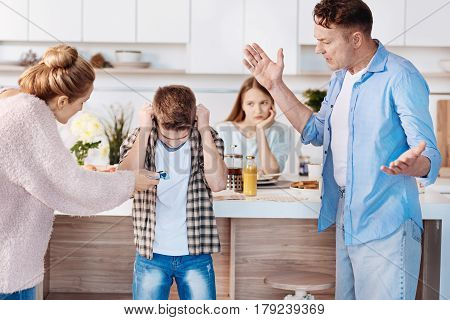 It is prohibited. Furious family couple holdign cigaretts and punishing their son while standing in the kitchen