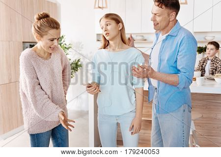 Difficalt age. Strict disappointed parents scolding their teenage daughter for bad bahavior while standing in the kitchen