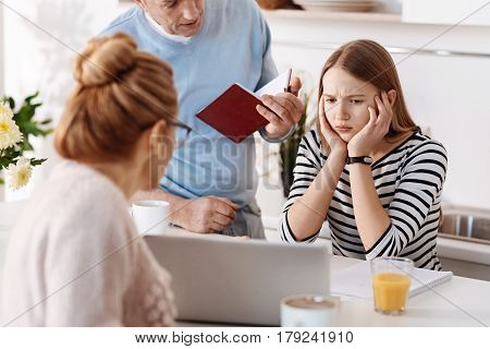 Just tired of it. Sad cheerless girl sitting at the table while her father helping her with homework