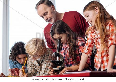 How can I help you. Charming inspiring committed man sharing some advice while children working on the research and conducting the experiment