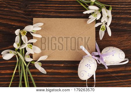 Traditional easter background with copyspace. Snowdrop flowers and easter eggs with blank label on brown wooden textured table.