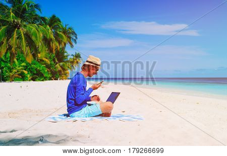 man with laptop and mobile phone on tropical beach, remote work