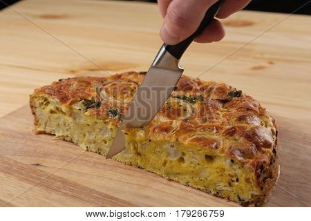 Man's hand with a knife cuts a kish pie on a wooden board