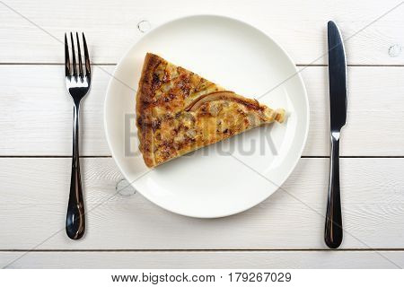 Tasty pie on a white plate with utlery lying on a white wooden table. Top view