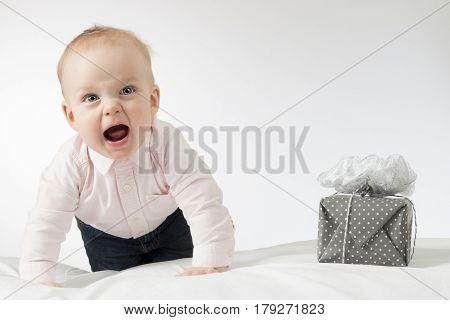 Screaming crawling infant baby looking at camera. Toddler kid with a gift on the white blanket. Horizontal stusio shot.