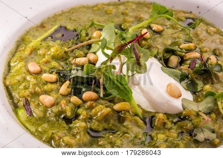 Orzotto with goat cheese and spinach with pine nuts and greens in a round plate