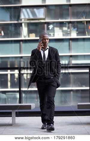 Full length portrait of a confident young businessman walking in the city talking on cell phone