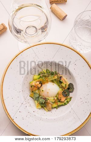 The served table with a dish from an asparagus with sauce ber-blan, goose egg and mussels. A glass of white wine with traffic jams on a white cloth