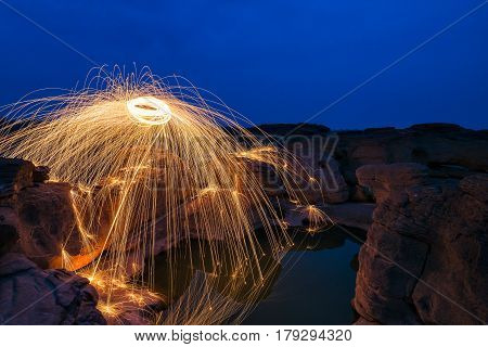 Long exposure capture of Burning steel wool being spun before dusk on a grand canyon rock field of Thailand