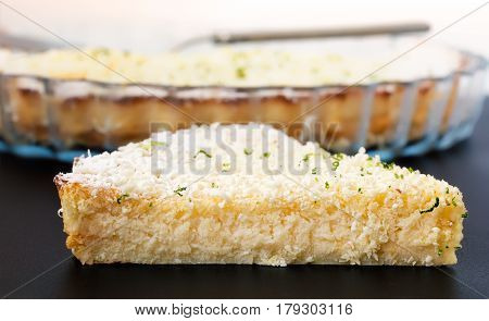 Lemon, lime, coconut impossible pie with white chocolate shavings slice with baking dish in the background