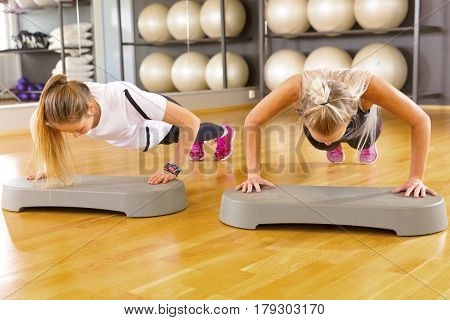 Full length portrait of confident female friends doing pushups in gym