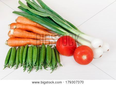 Green fresh onionred tomatocarrot and peas on the white wooden background.