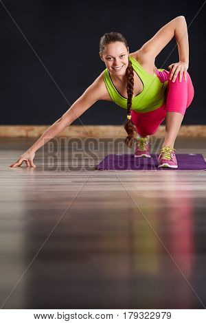 Young slim woman in yoga class making beautiful asana exercises. Healthy lifestyle in fitness club. Woman in the sportwear, pink legginga and green t-shirt. In the yogastudio on the violet yoga mat.