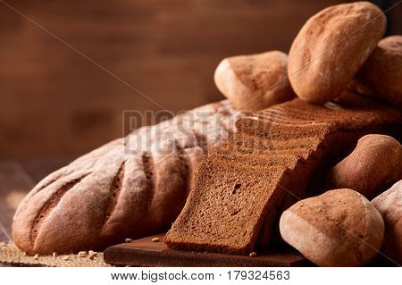Freshly baked bread loaves on burlap on wooden table with brown blurred background. Texture closeup bakery products. Wheat. Slice of bread on the board.